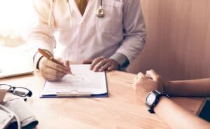 A doctor handling a chronic illness chart fills out a form for their patient.