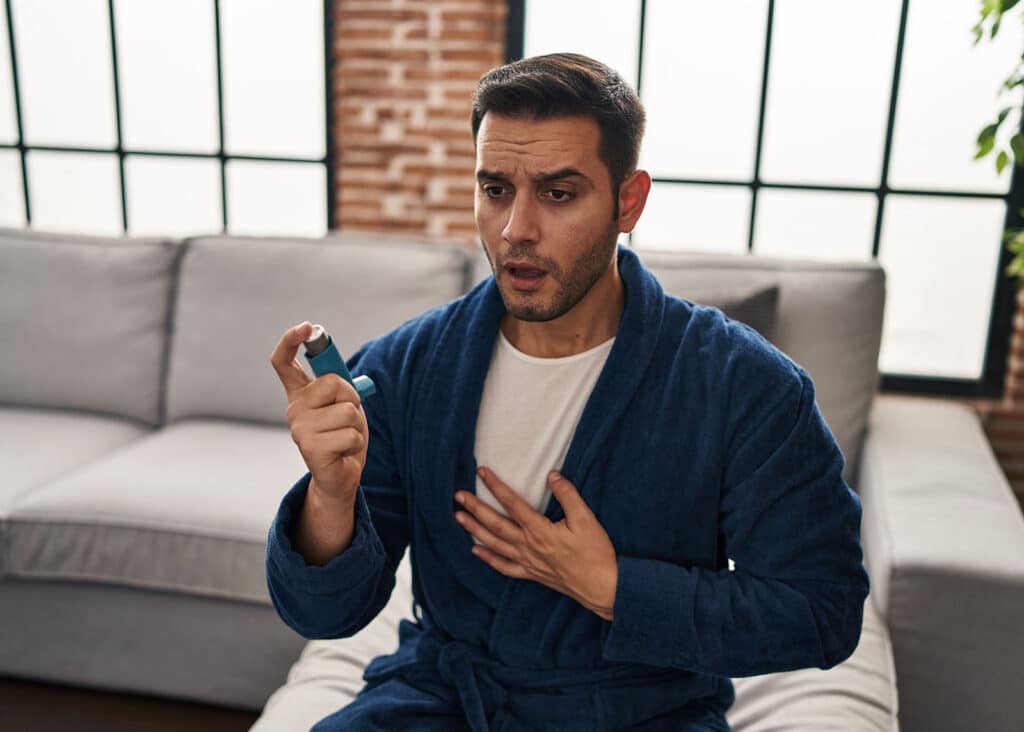 A man uses Asmanex as his inhaler sitting on the couch in his living room.